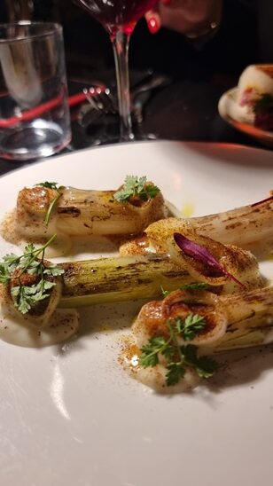 Piatto bianco di eramica su tavolo di un ristorante con porri cotti e salse
