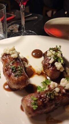 Bonbette di carne su piatto di ceramica bianca con calice di vino rosso sullo sfondo