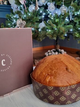 panettone intero con accanto confezione in cartone marrone e sullo sfondo albero di natale