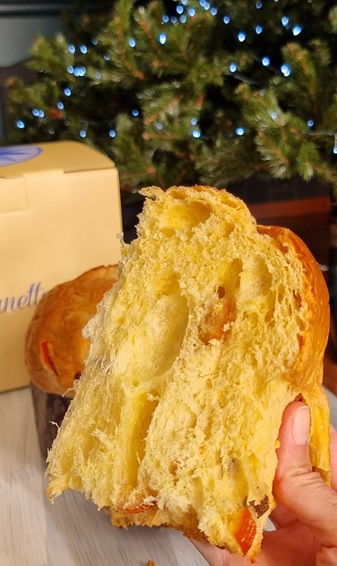 Fetta di panettone classico in una mano e sfondo con confezione di cartone e luci di natale