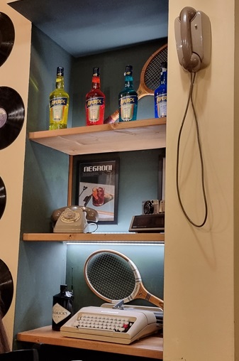 parete con oggetti vintage da Glory POP pizzeria Milano, macchina da scrivere Olivetti, bottiglie Aperol, libro Negroni, telefoni a ghiera