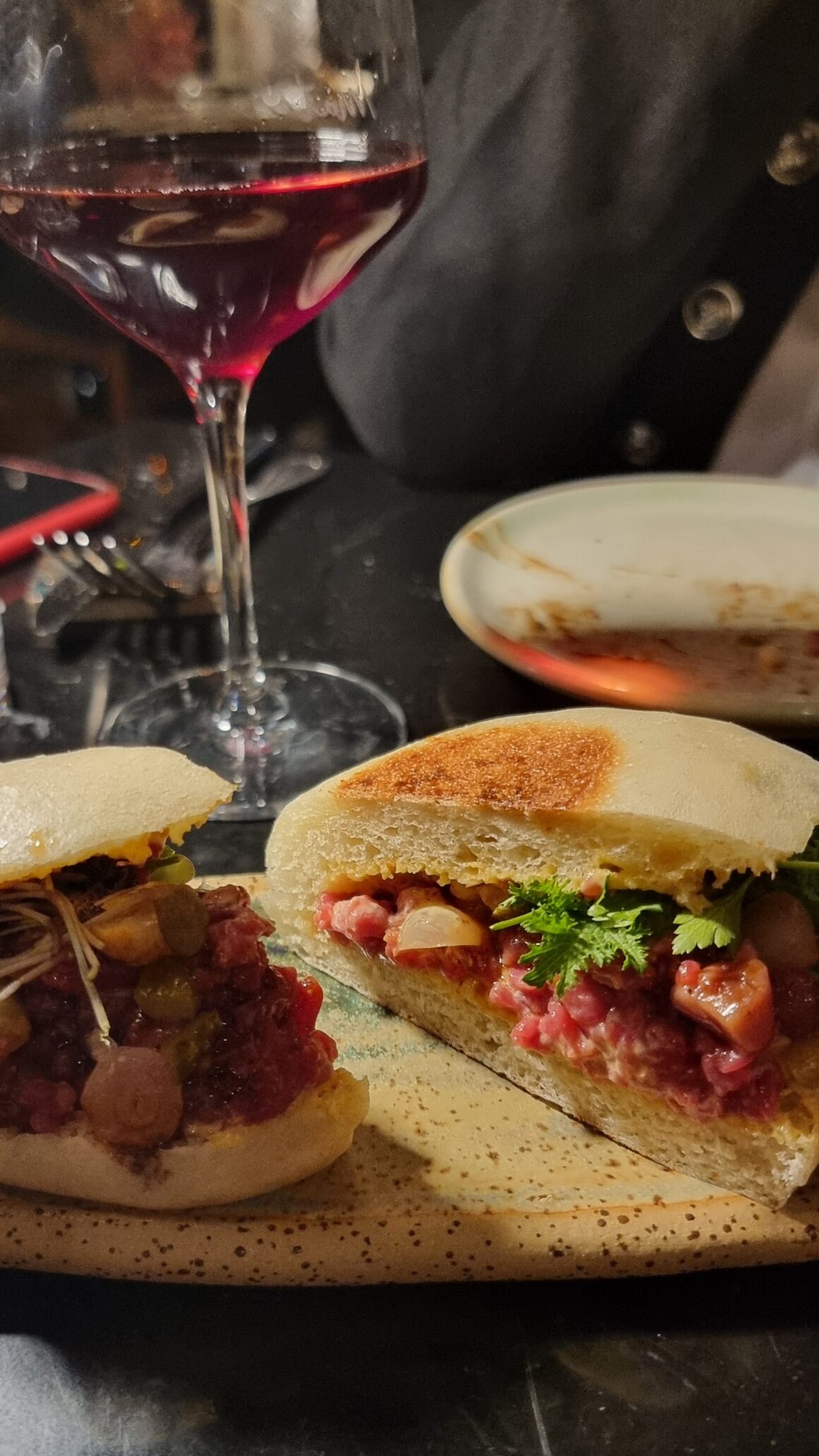 panino ripieno di tartare di manzo con verdure in un piatto su un tavolo scuro in un ristorante con bicchiere di vino rosso sullo sfondo