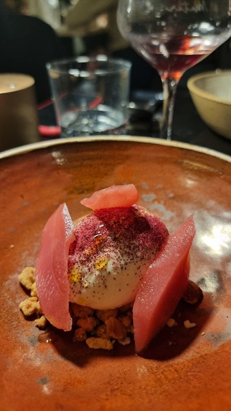Piatto di ceramica marrone con dessert di pere cotte nell'ibisco e cremoso di cioccolato bianco su tavolo in un ristorante