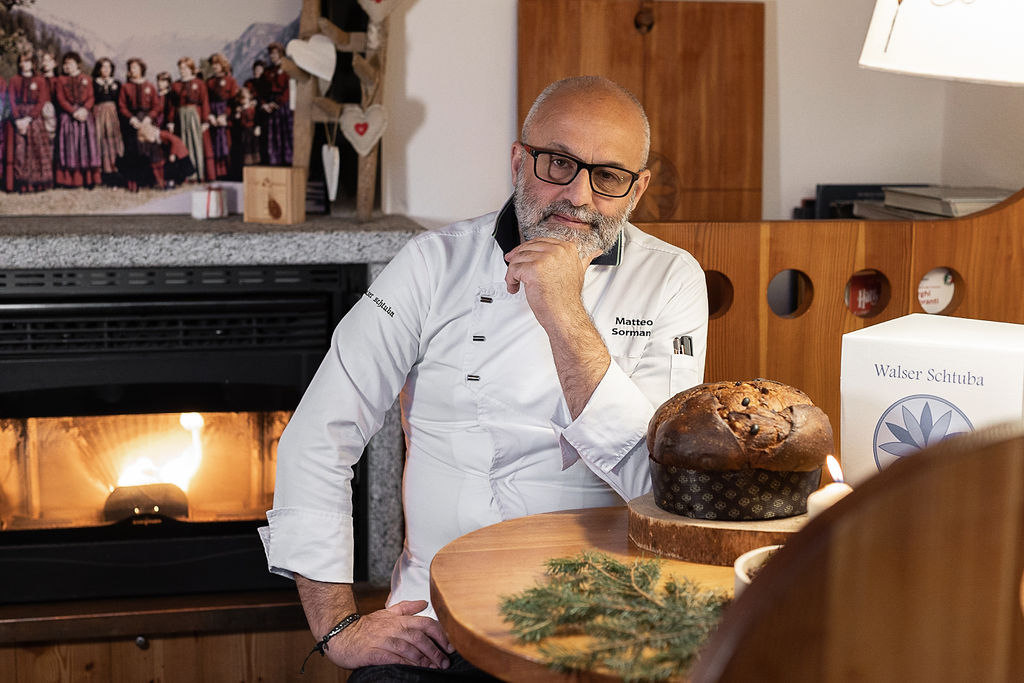 Matteo Sormani seduto a un tavolo con camino sullo sfondo e il panettone sul tavolo