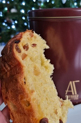 fetta di panettone in mano e in secondo piano scatola di latta confezione