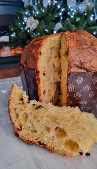 panettone con fetta tagliata in primo piano e albero di natale decorato con luci sullo sfondo